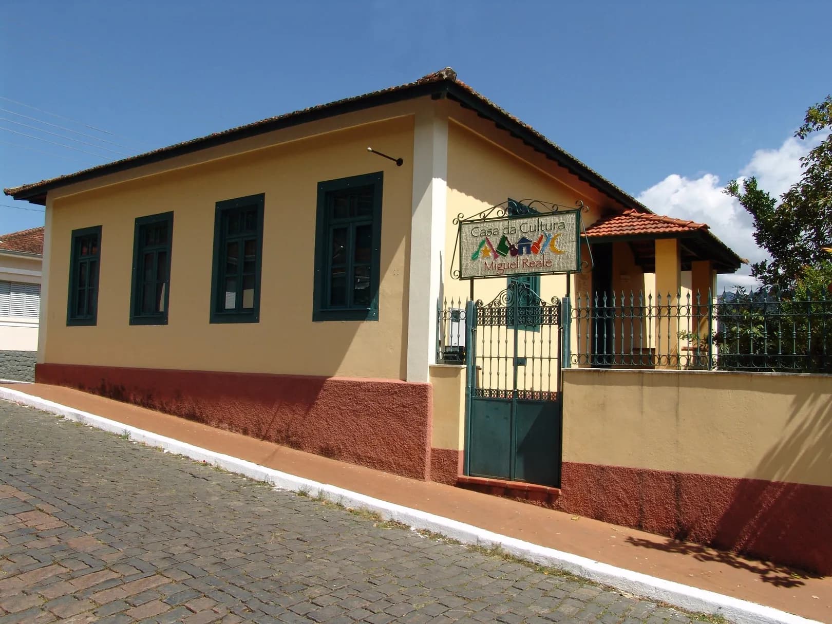 Fachada amarela da Casa da Cultura Miguel Reale, com janelas verdes e portão de ferro na rua de paralelepípedo
