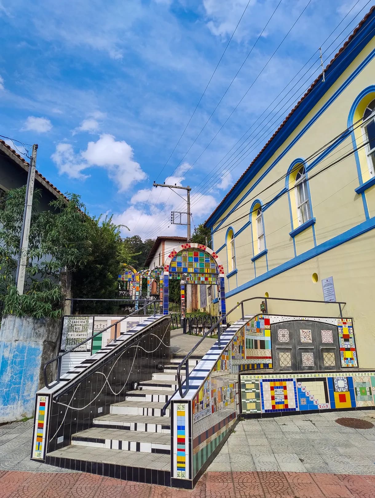 Escadaria da Ladeira dos Pirilampos revestida de mosaico, com corrimão de ferro e os arcos coloridos ao fundo